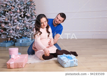 A happy husband and wife are preparing to become parents, having fun near the Christmas tree. Pregnancy and Christmas A happy husband and wife are preparing to become parents, having fun near the Christmas tree. Pregnancy and Christmas 94193509