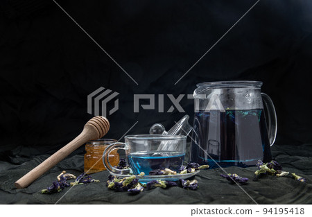 Butterfly pea tea (Clitoria) or Organic blue anchan in Teapot and glass cup served with honey on Dark background. 94195418