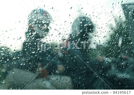 Motorcycle riders in the rain through a window with rain drops 94195617