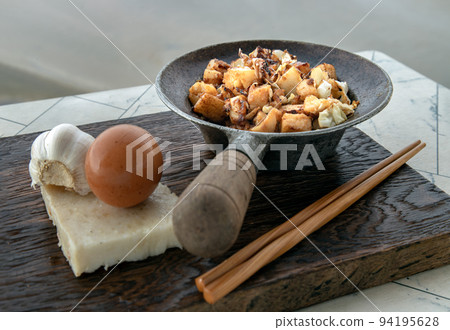 Traditional stir fried soft turnip cake or Fried radish cake (chai tow kway) in small steaming iron pot Served with wooden chopsticks on white table. 94195628