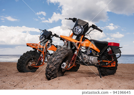 Two custom off-road sports motorcycles are parked on beach outdoors 94196645