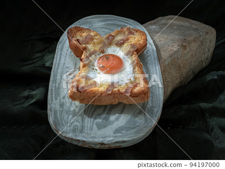 Homemade fried egg in a hole Bacon and Cheese toast on ceramic tray with dark background. 94197000