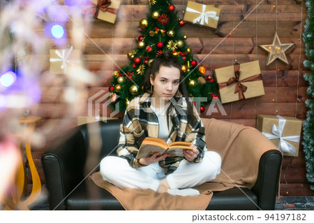 A young girl is reading a book comfortably sitting on the sofa on New Year's Eve 94197182