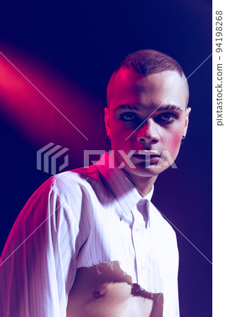 Close-up portrait of young man wearing makeup, smokey eyes, posing isolated over purple background in neon light 94198268