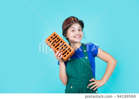 labour day. Little girl bricklayer. learning how to build. Little worker in helmet building from brick. Architecture construction child. Child in uniform working around brick wall 94199569
