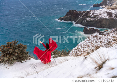 Woman in a red dress high in the snowy mountains by the emerald lake 94199818