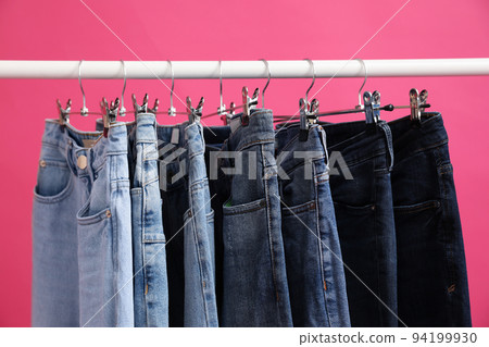 Rack with stylish jeans on pink background, closeup Rack with stylish jeans on pink background, closeup 94199930