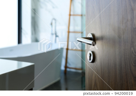 wooden door open to nice modern bathroom, marble walls. selective focus to door handle, bathroom and bathtub blurred on background. wooden door open to nice modern bathroom, marble walls. selective focus to door handle, bathroom and bathtub blurred on background. 94200019