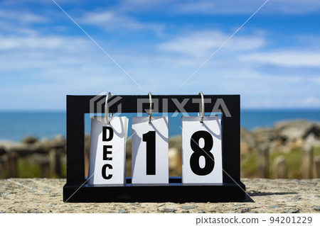 Dec 18 calendar date text on wooden frame with blurred background of ocean. 94201229