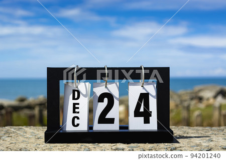 Dec 24 calendar date text on wooden frame with blurred background of ocean. 94201240
