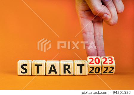 2023 start new year symbol. Businessman turns a wooden cube and changes words Start 2022 to Start 2023. Beautiful orange table orange background, copy space. Business 2023 start new year concept. 94201523