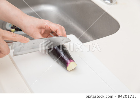 [A middle-aged housewife prepares to cut eggplant into strips with a Santoku knife] 94201713