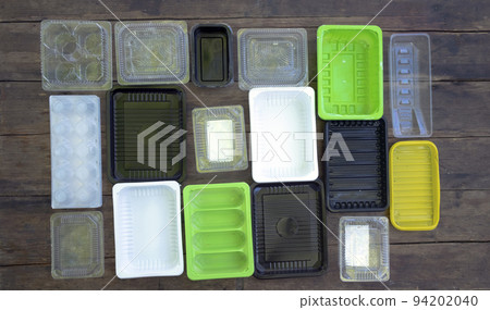 Multi-colored disposable plastic food containers are laid out on a wooden floor. plastic pollution 94202040