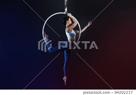 Young woman performing acrobatic element on aerial ring indoors Young woman performing acrobatic element on aerial ring indoors 94202217