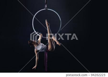 Young woman performing acrobatic element on aerial ring indoors Young woman performing acrobatic element on aerial ring indoors 94202223