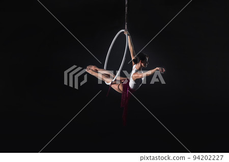 Young woman performing acrobatic element on aerial ring indoors Young woman performing acrobatic element on aerial ring indoors 94202227