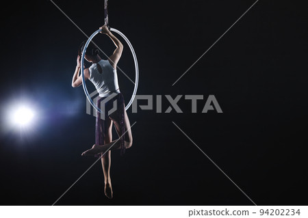 Young woman performing acrobatic element on aerial ring against dark background. Space for text Young woman performing acrobatic element on aerial ring against dark background. Space for text 94202234
