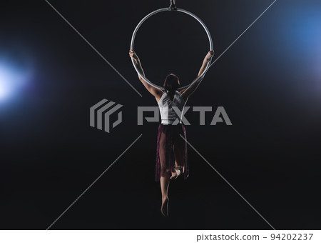 Young woman performing acrobatic element on aerial ring indoors Young woman performing acrobatic element on aerial ring indoors 94202237