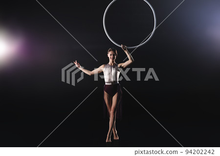 Young woman performing acrobatic element on aerial ring indoors Young woman performing acrobatic element on aerial ring indoors 94202242
