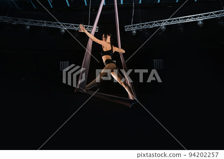 Young woman performing acrobatic element on aerial silk indoors 94202257