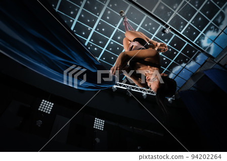 Young woman performing acrobatic element on aerial silk indoors, low angle view Young woman performing acrobatic element on aerial silk indoors, low angle view 94202264