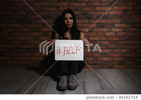 Abused young woman showing palm with word HELP against black background, focus on hand 94202724