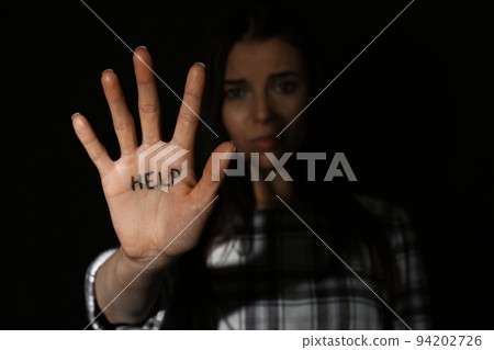 Abused young woman showing palm with word HELP against black background, focus on hand 94202726