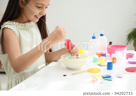 Cute little girl mixing ingredients with silicone spatula at table in room. DIY slime toy 94202733