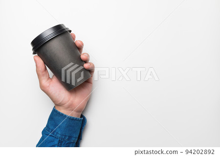 A man's hand in a shirt holds a paper black cup of coffee on a white background A man's hand in a shirt holds a paper black cup of coffee on a white background 94202892