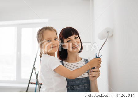 Happy family mother and daughter paint the wall with white paint. 94203014