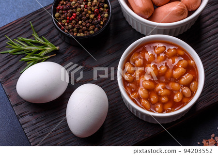 Traditional English breakfast with eggs, toast, sausages, beans, spices and herbs on a grey ceramic plate 94203552