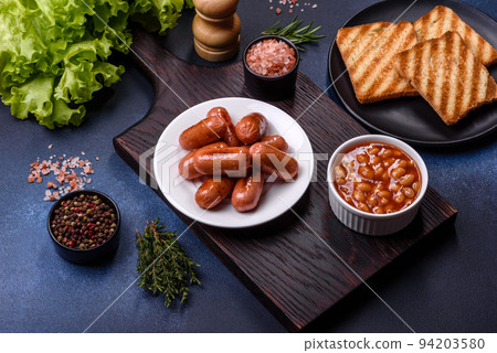 Traditional English breakfast with eggs, toast, sausages, beans, spices and herbs on a grey ceramic plate 94203580