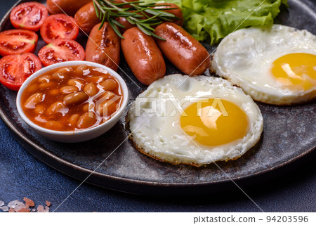 Traditional English breakfast with eggs, toast, sausages, beans, spices and herbs on a grey ceramic plate Traditional English breakfast with eggs, toast, sausages, beans, spices and herbs on a grey ceramic plate 94203596