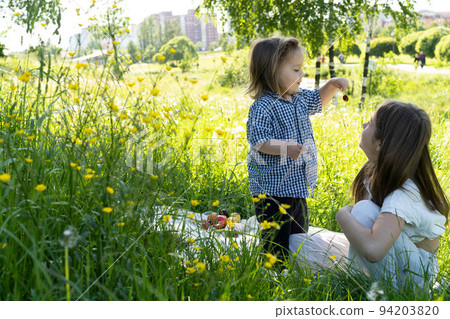 Brother and sister are playing in the park among the green grass. Brother feeds sister. Picnic outside the city. Childhood. Relationships. Brother and sister are playing in the park among the green grass. Brother feeds sister. Picnic outside the city. Childhood. Relationships. 94203820