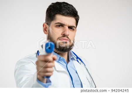 Doctor man in white medical coat directs electronic non-contact thermometer into camera lens and Doctor man in white medical coat directs electronic non-contact thermometer into camera lens and 94204245