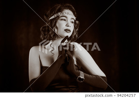 Woman dressed in Roaring twenties era with feathers boa on dark background. Retro, party, fashion Woman dressed in Roaring twenties era with feathers boa on dark background. Retro, party, fashion 94204257