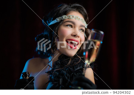 Retro styled woman dressed in Flappers dress raises glass of champagne like toast, drinking wine on 94204302