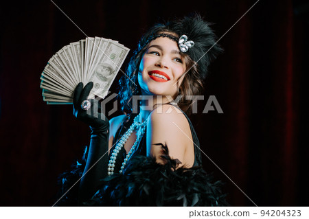 Rich luxurious woman dressed in Gatsby style waves a bundle of dollars banknotes like fan. Vintage Rich luxurious woman dressed in Gatsby style waves a bundle of dollars banknotes like fan. Vintage 94204323