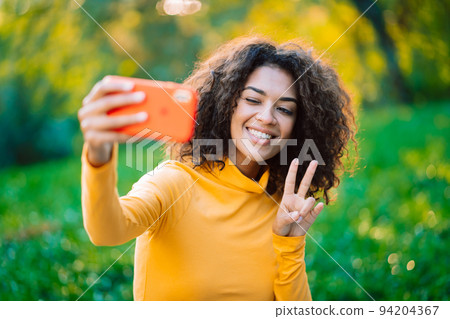 Beautiful african american woman holding and using smart phone to film herself outdoor. Black female Beautiful african american woman holding and using smart phone to film herself outdoor. Black female 94204367