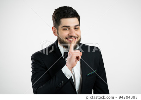Man with beard in tuxedo holding finger on lips over white background. gentleman making gesture of 94204395