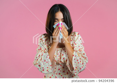 Woman sneezes into tissue. Isolated girl on pink studio background. Lady is sick, has a cold or Woman sneezes into tissue. Isolated girl on pink studio background. Lady is sick, has a cold or 94204396