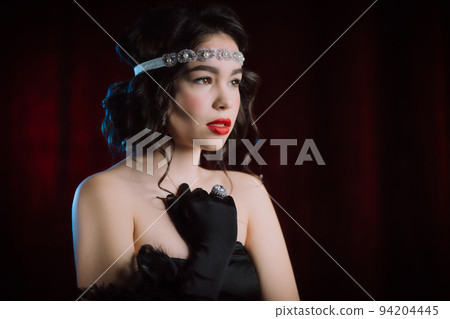 Old-fashioned woman dressed in style of Flappers posing on dark red background. Roaring twenties Old-fashioned woman dressed in style of Flappers posing on dark red background. Roaring twenties 94204445