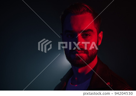 Portrait of young caucasian man with beard in leather jacket illuminated neon light looking at 94204530