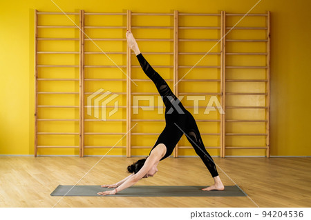 Young woman in yellow class space doing stretching legs. Yoga coach in black practicing at light 94204536
