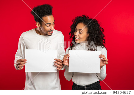 Portrait of young smiling african american man and woman couple holding white empty paper blanks on 94204637