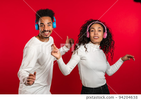 Young african american couple dancing with headphones isolated on red background studio. Party Young african american couple dancing with headphones isolated on red background studio. Party 94204638