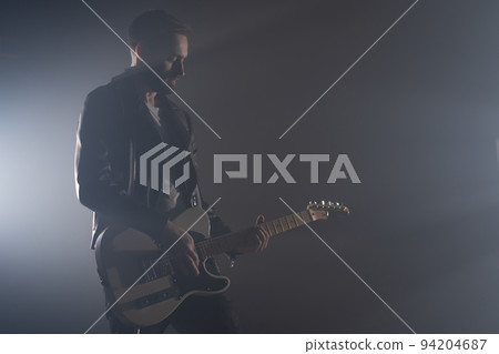 Rock guitarist man in leather jacket in smoky studio or stage masterfully playing electric guitar 94204687