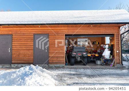 Facade view open door ATV home garage with quad bikes offroad vehicle parked sunny snowy cold winter day. ATV adventure extreme sport. House organized clutter warehouse tools equipment shed storage Facade view open door ATV home garage with quad bikes offroad vehicle parked sunny snowy cold winter day. ATV adventure extreme sport. House organized clutter warehouse tools equipment shed storage 94205451