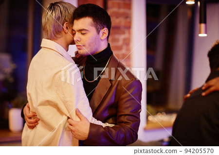 Young couple of boyfriends in smart casualwear standing in embrace Young couple of boyfriends in smart casualwear standing in embrace 94205570