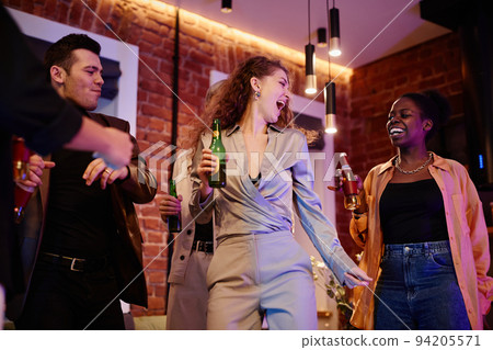 Happy young woman in grey suit with bottle of beer dancing among friends 94205571